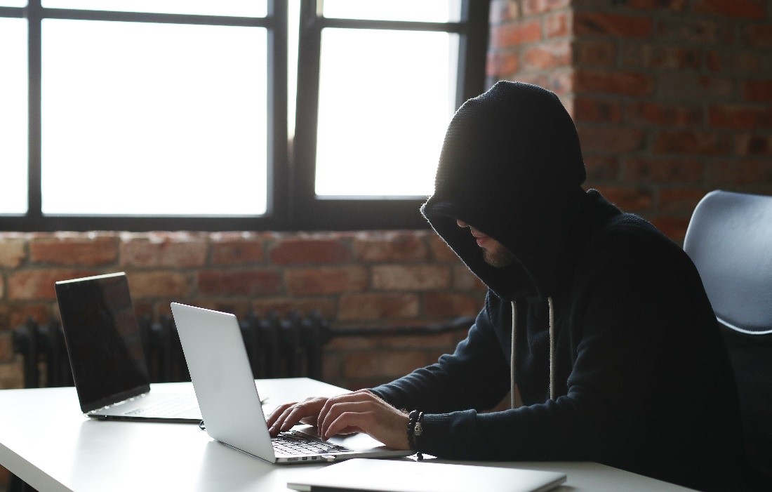 A hooded man is typing on his laptop